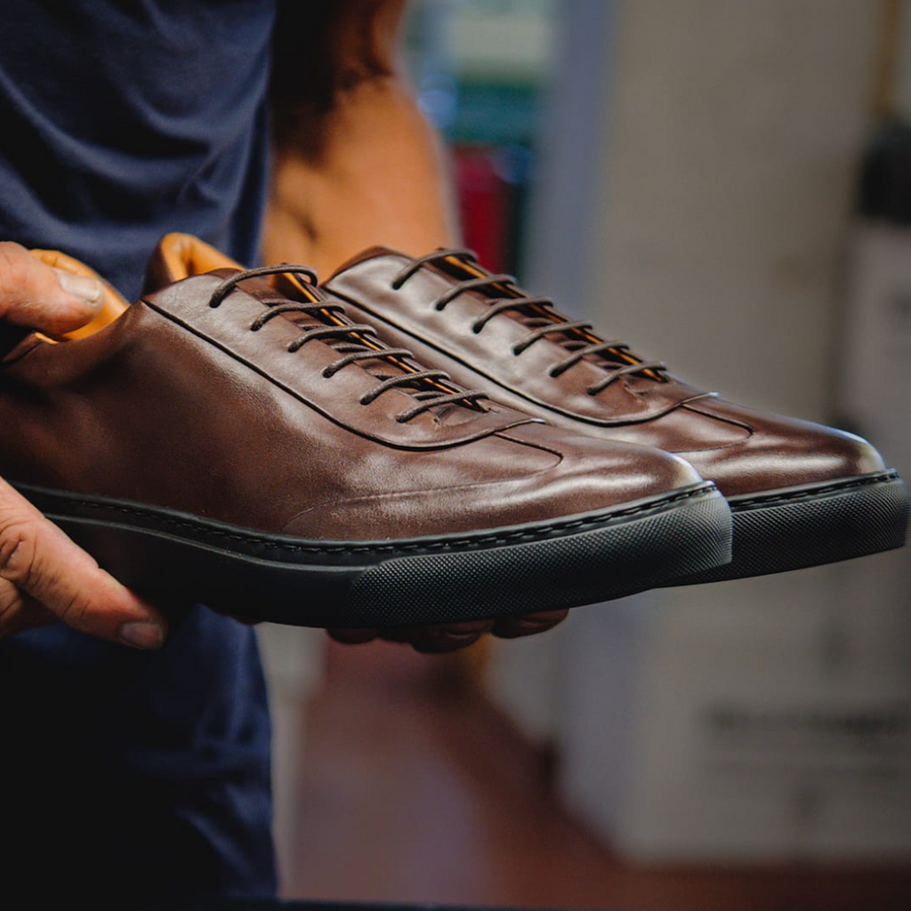 Artisan in Italy holding finished brown sleek leather dress sneakers for men
